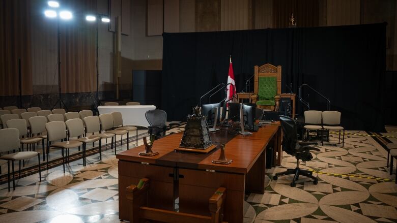 A makeshift House of Commons is set up in a building across from parliament. A formal Speaker's chair and clerk's table is seen in the aisle. Stackable chairs where MPs would sit line the aisle.