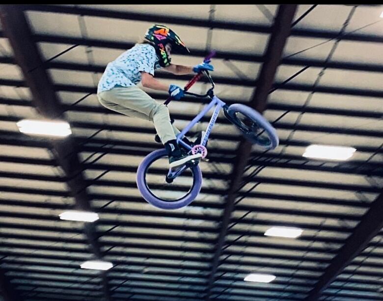 A boy on a BMX bike sails high in the air inside a large facility.