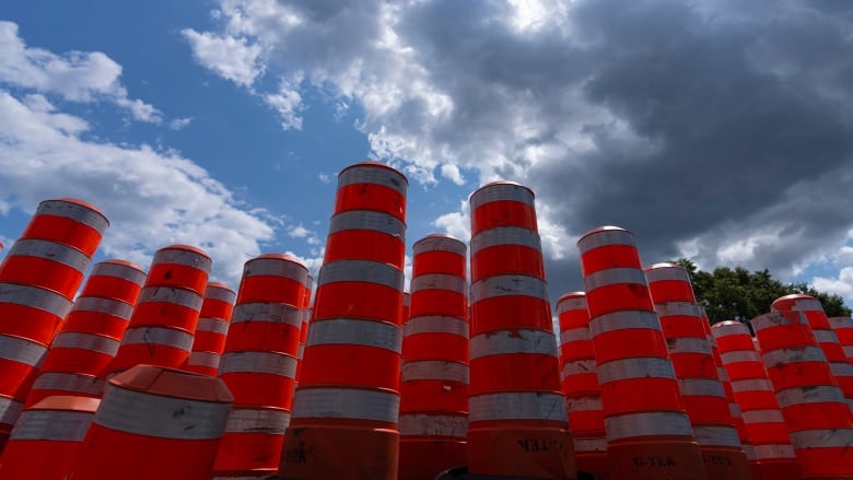 Large orange traffic cones assembled against blue sky and white clouds.