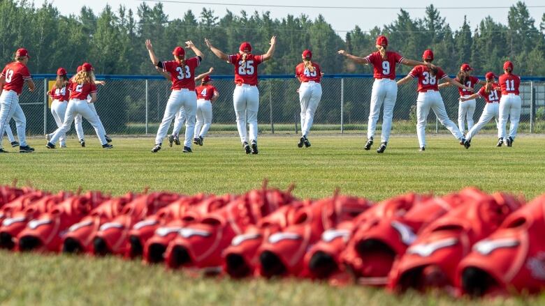 The Canadian national women's baseball team does jumping jacks on a baseball field.