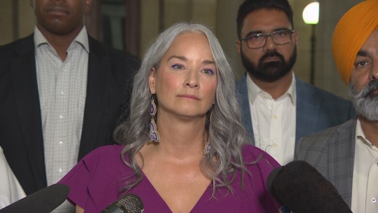 A woman in purple speaks to the media, flanked by some of her colleagues. 