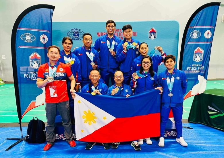 Athletes from the Philippines are dressed in their uniforms and holding a Philippines flag as they show off their medals.