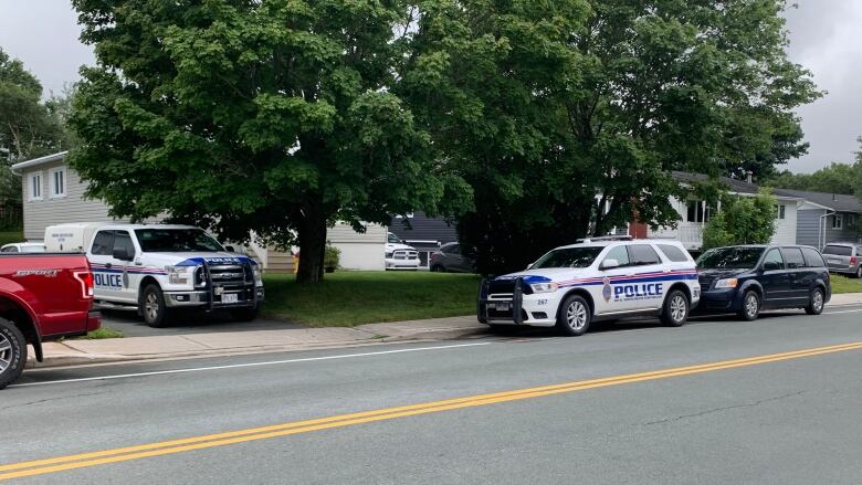 Police vehicles are parked in the driveway and on the street outside a home on a residential street.