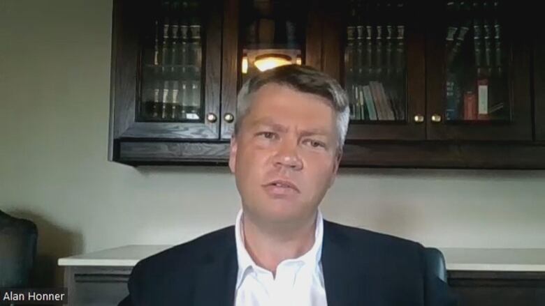 Alan Honner sits in front of a bookcase with glass doors