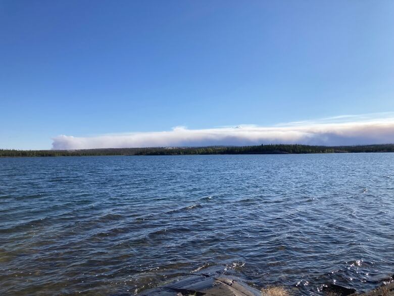 A plume of smoke over some trees and a lake. A wildfire burning about 40 kilometres southeast of Dettah, N.W.T., as seen from Reid Lake on Monday.