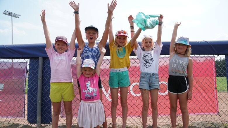 Six young girls stand along a fence and throw their arms up in the air.