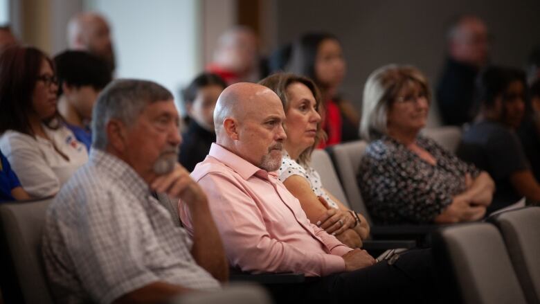 A man in a pink shirt sits in a row of seating