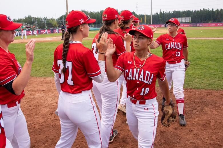 Baseball players wearing red Canada jerseys high-five on a field.