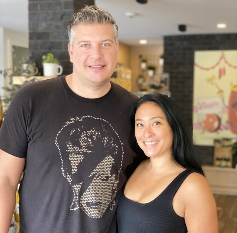 A man in a black tee-shirt stands with his arm around the waist of a woman in a black dress.