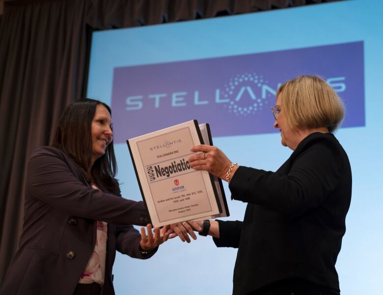 Two woman shake hands while holding a binder