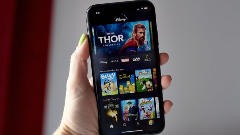 A woman's hand holds a smartphone with the Disney+ app open