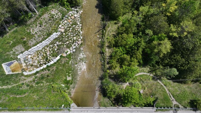 An above shot of a swath of green land, running water and piles of stones.