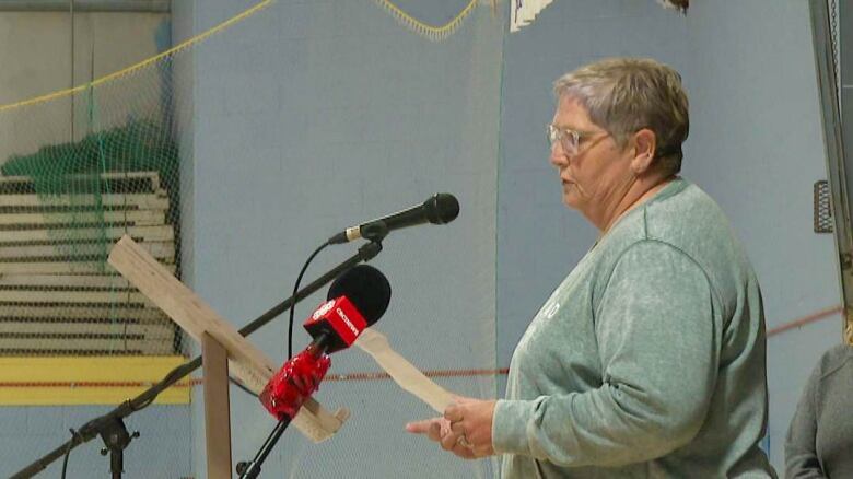 An elderly woman with a green sweater speaks at a microphone