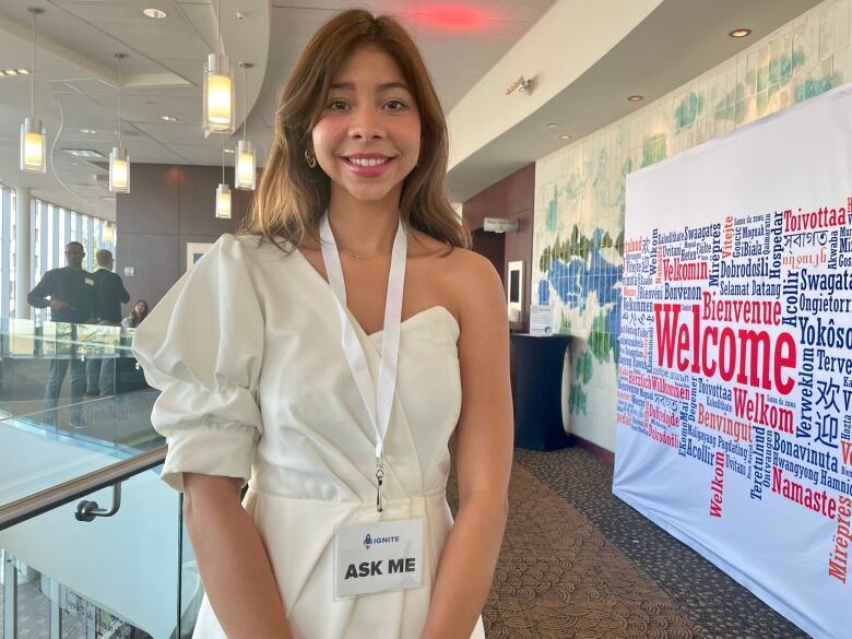 A lady wearing an ask me tag, standing besides an event banner.