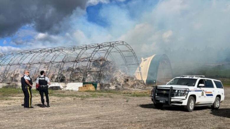 Wide shot of police officers on the scene near the skeleton of a burned-out barn.