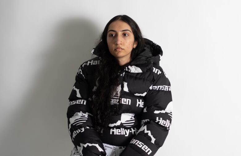 Rapper Lioness Kaur, sits on a black stool against a white background wearing white and black clothing.