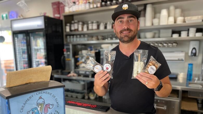 A man smiles as he holds several ice cream bars behind a counter.