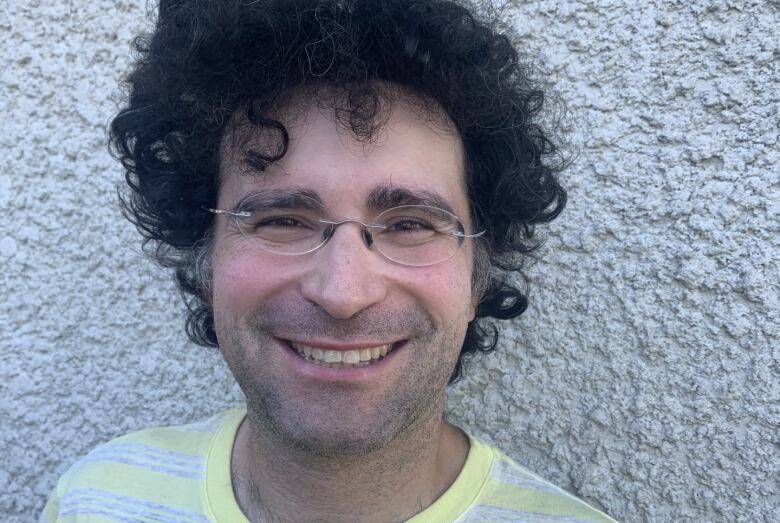 A man wearing glasses and a striped shirt smiles in front of a wall.