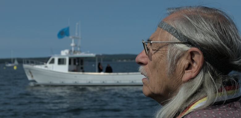 A man looks left, and we see the side of his face. The boat passes by in the background.