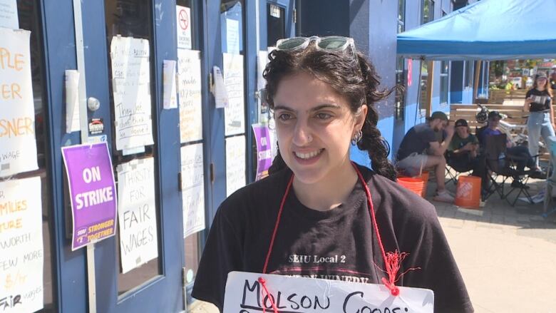 A woman with braided black hair wearing a sandwich board smiles.