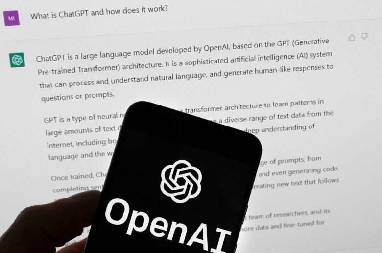  A hand holds up a smartphone with a black screen with the words OpenAI in white.