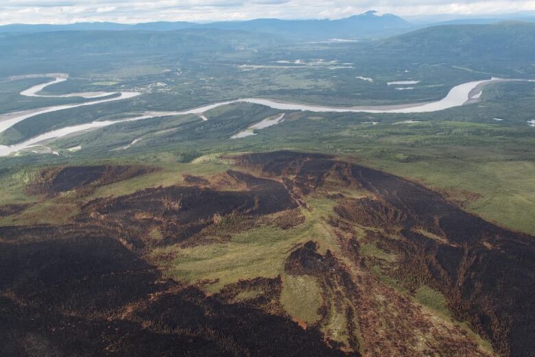 Aerial view of a burned hillside with a river and village visible in the distance.