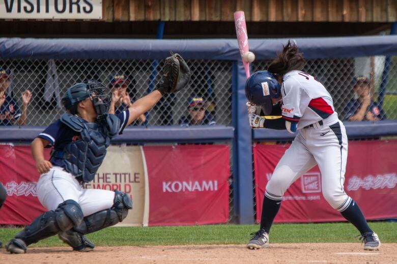 A baseball player ducks a pitch at home plate.