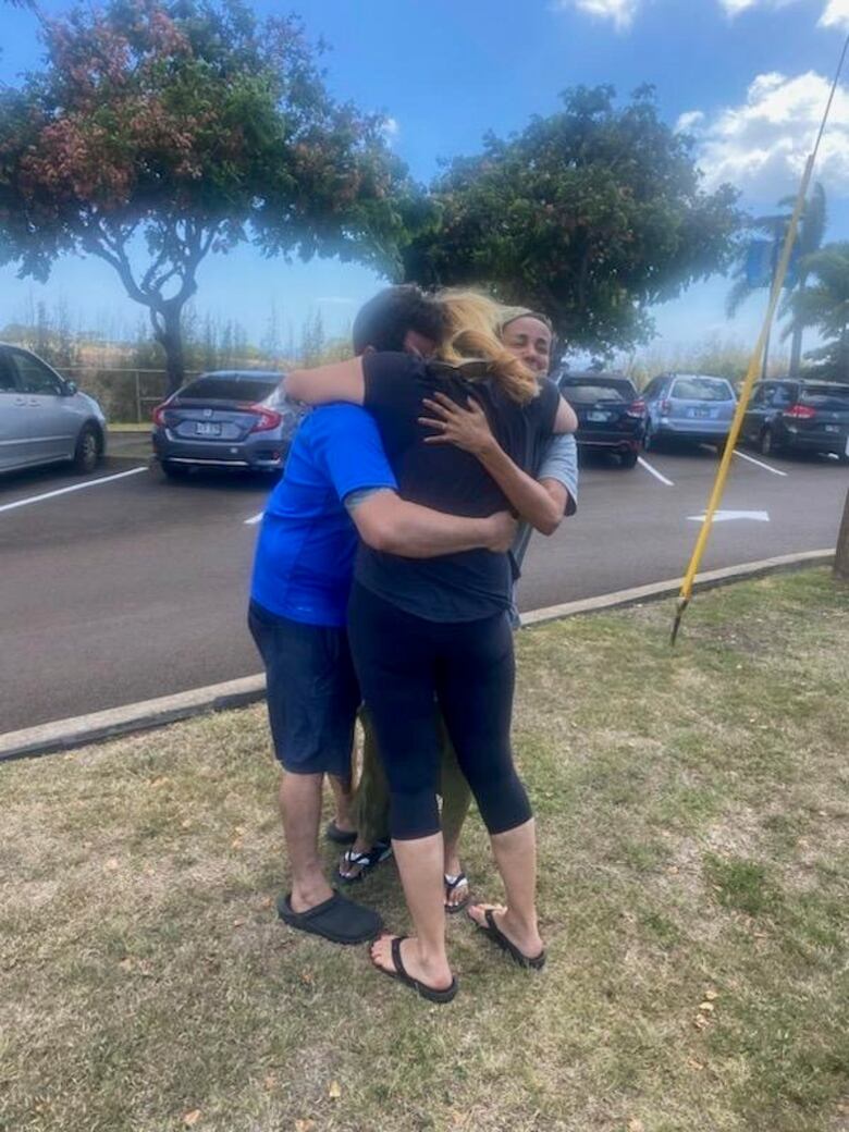 Three people hug near some palm trees.