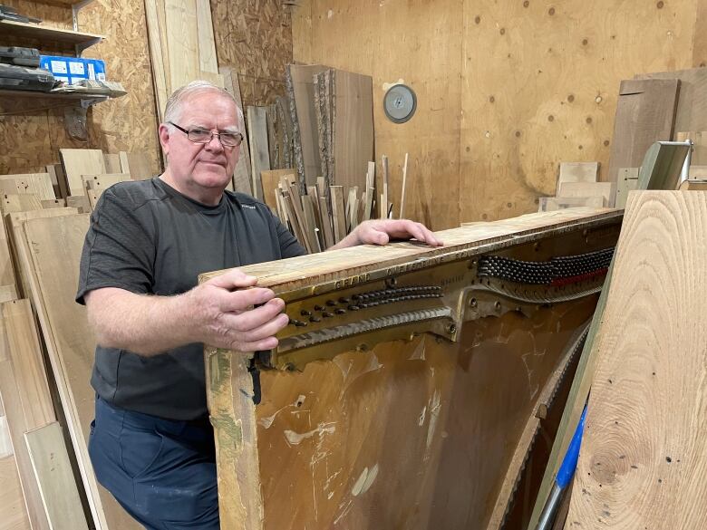 A man with grey hair and glasses holds a deconstructed piano