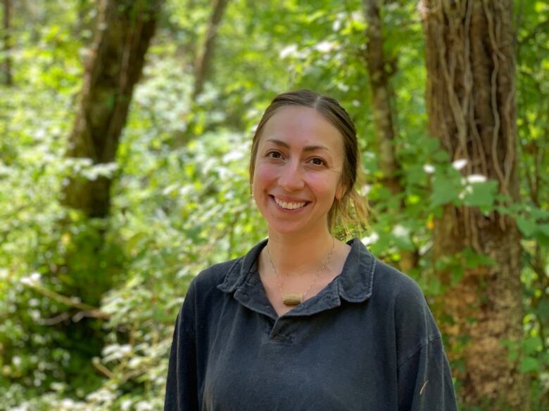 A smiling woman stands in a green forest. 