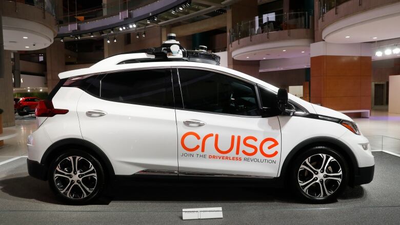 A white car with a bright orange Cruise logo on the door and the words 