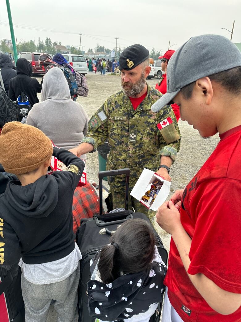 A man in army gear hands out chocolate bars to kids.