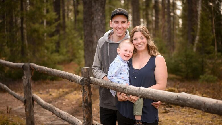 A woman smiles carrying her son, next to her a man stands with his arm around her waist. 