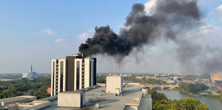 Black smoke comes from the top of an apartment building, with river and human rights museum in the background.