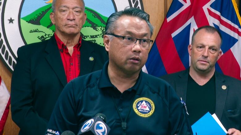 A person in glasses wearing a uniformed shift speaks at a microphone.