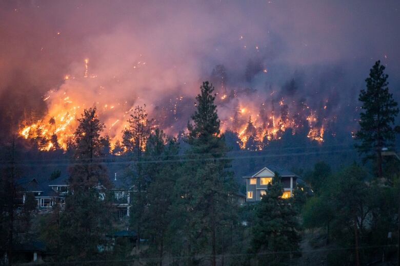 A wildfire burns near a home in the city of Kelowna, British Columbia on Friday, August 18, 2023. 