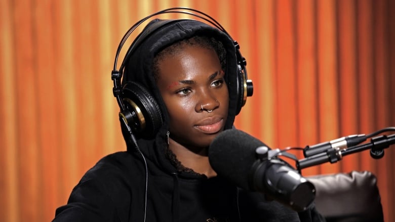 Haviah Mighty sitting in front of a studio microphone against a wood-panelled wall.