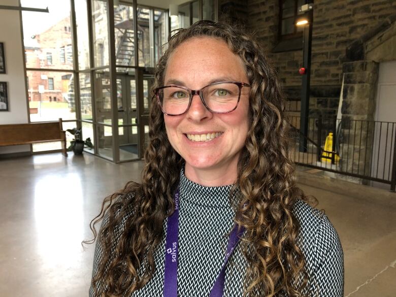 Smiling young woman with long brown curly hair and brown glasses wearing white and black dress and lanyard around her neck.