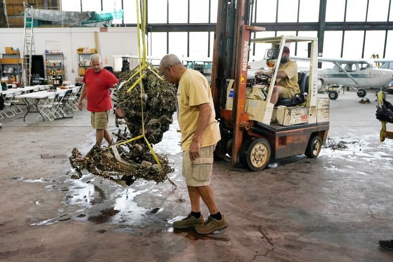 Two men walks alongside a piece of equipment in a large room