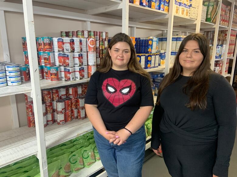 Two people, one wearing a t-shirt featuring a heart-shaped Spiderman logo, stand in front of shelves of food.