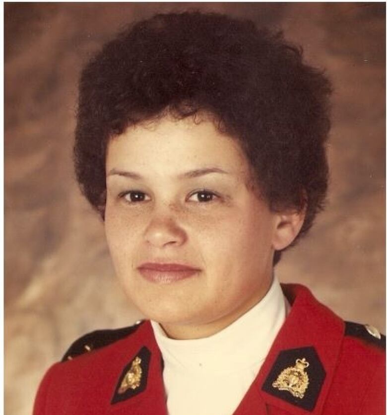 A head shot of a young woman with a short afro haircut in a red serge RCMP dress uniform.