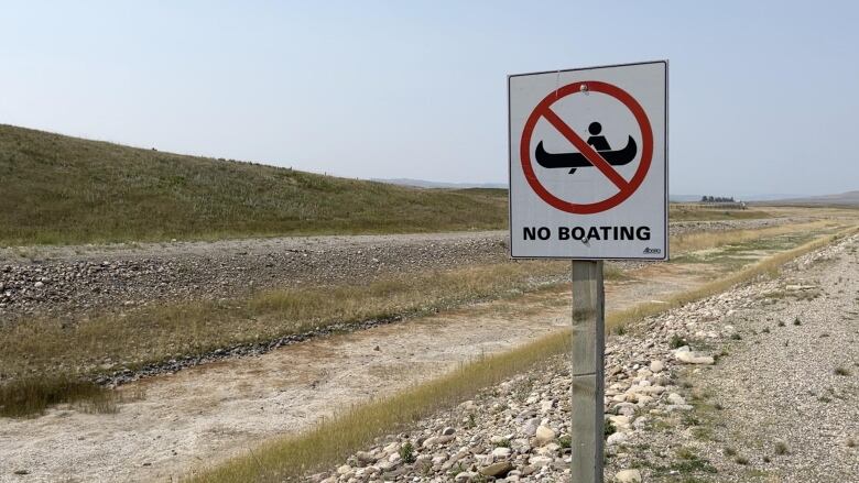 A canal from the Pine Coulee reservoir is dry. A sign next to the canal says boating is not allowed. 