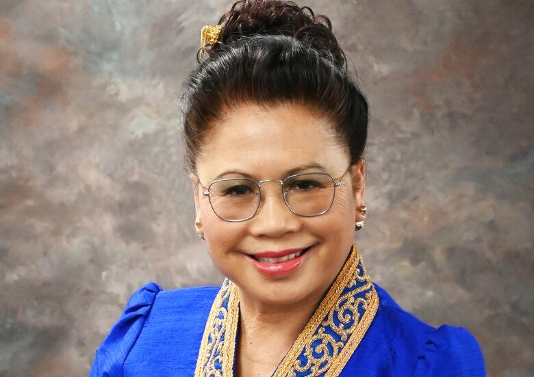 A woman in a royal blue garment with an embroidered collar smiles for a photograph. 