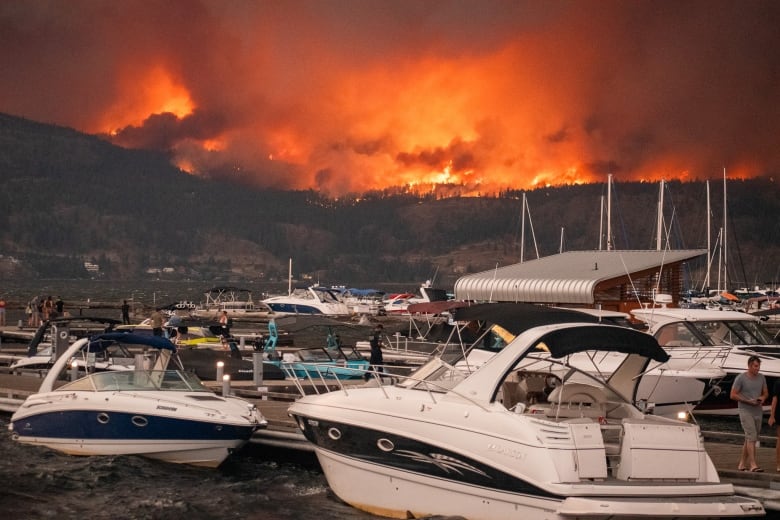 Boats on a lake are pictured against wildfires in the mountain across.