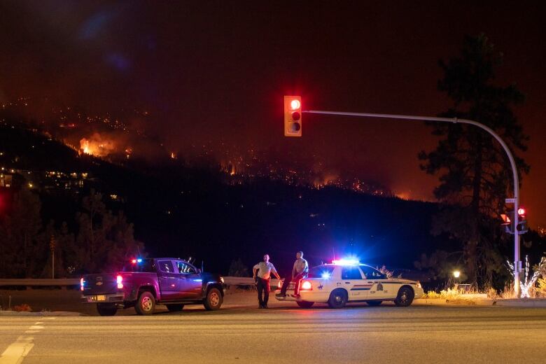 Two officers sit on police vehicles as a wildfire rages behind them.