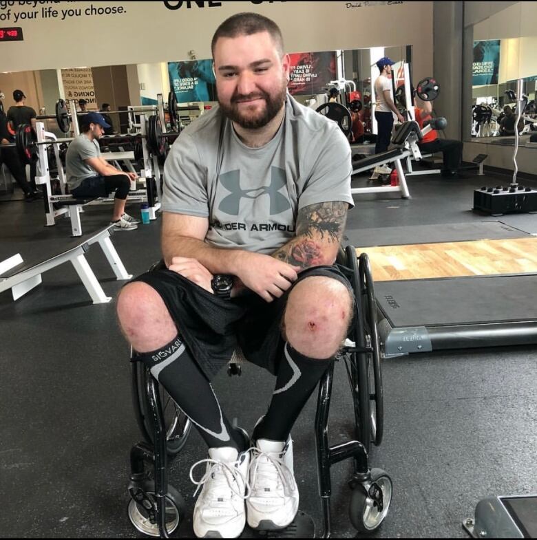 A man sitting in a wheelchair, smiling at the camera inside a gym.