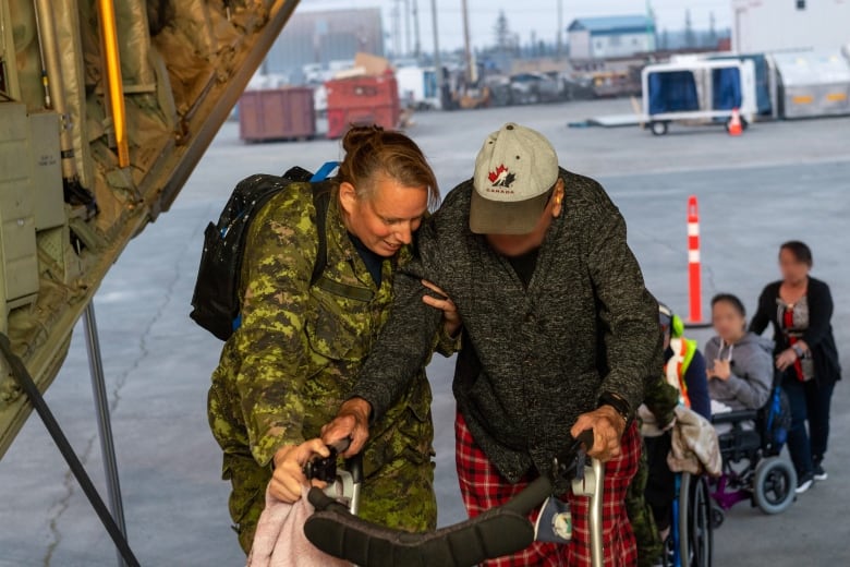 A woman dressed in camouflage helps a man through the loading door of a cargo plane.