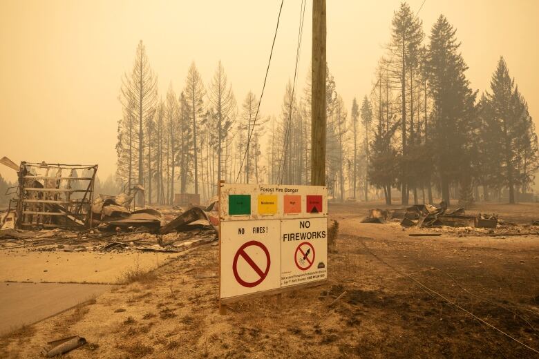 A sign showing an extreme wildfire warning stands amidst rubble.