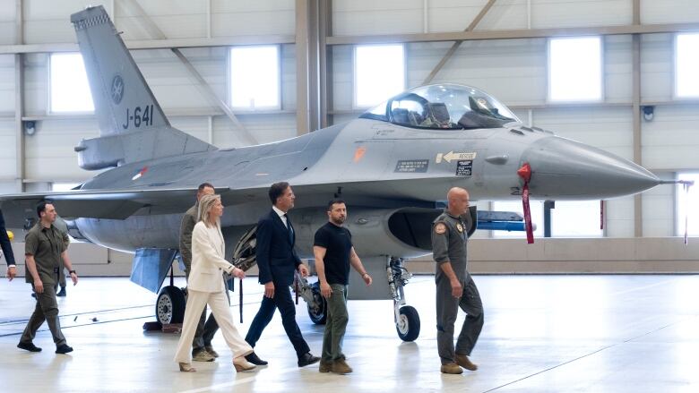 People walk past an F-16 fighrer jet at a military air base.