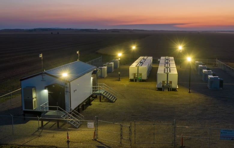 An small industrial facility in a rural field, with a setting sun behind it.